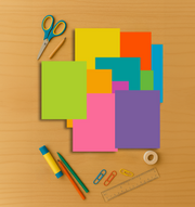 8.5” x 11” bright cardstock in 10 vibrant colors arranged on a wooden surface with scissors, pencils, and paper clips.