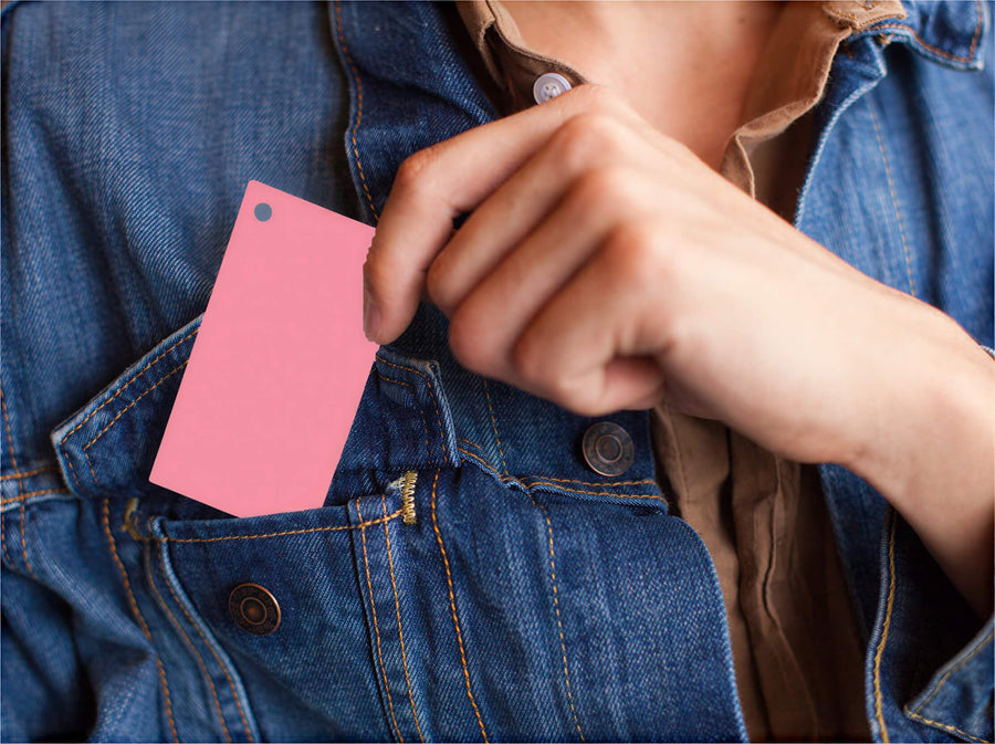 Blank pink index card being held in a hand, with a hole punch, against a denim jacket background.