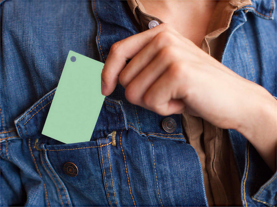 Green 2” x 3.5” blank index card with a hole punch, held in a person's hand near a denim jacket pocket.