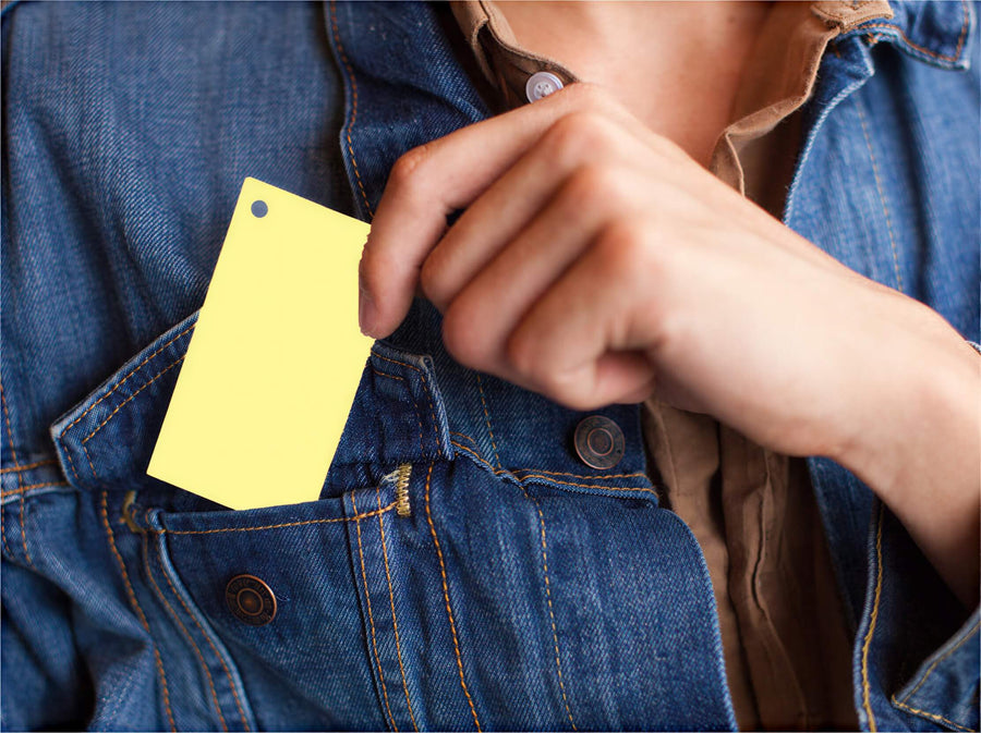 Yellow 2” x 3.5” blank index card with a hole punch, held in a person's hand near a denim jacket pocket.