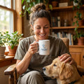 A woman holding a white ceramic mug with an Animal Health Alliance logo while sitting with a golden dog.