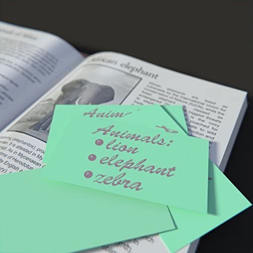 Mini blank index cards in assorted colors, placed on an open book about elephants, featuring handwritten notes.